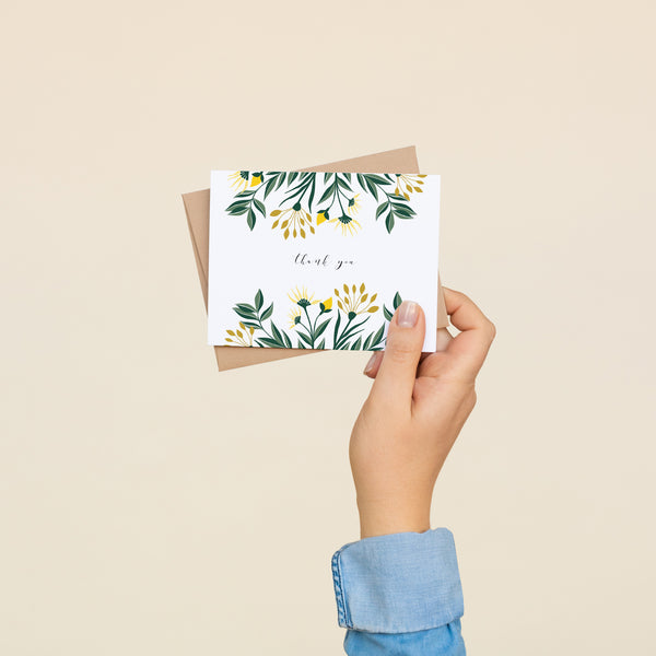 Single folded A2 greeting card with an envelope with an illustration of yellow aster flowers and green leaves sprouting from the top and bottom of the card. In the center is text in cursive that states "Thank You".