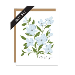 Box set of 8 folded A2 greeting cards with envelopes with an illustration   of blue dogwood flowers and green leaves. Text below and to the right of the bouquet states "Thank You" in cursive.