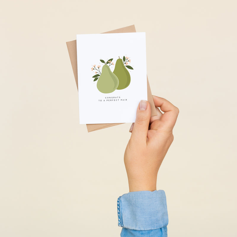 Single folded A2 greeting card with an envelope with an illustration of two pears in the center of the card with small pink flowers blooming from them. Below the pears state "Congrats To A Perfect Pair".