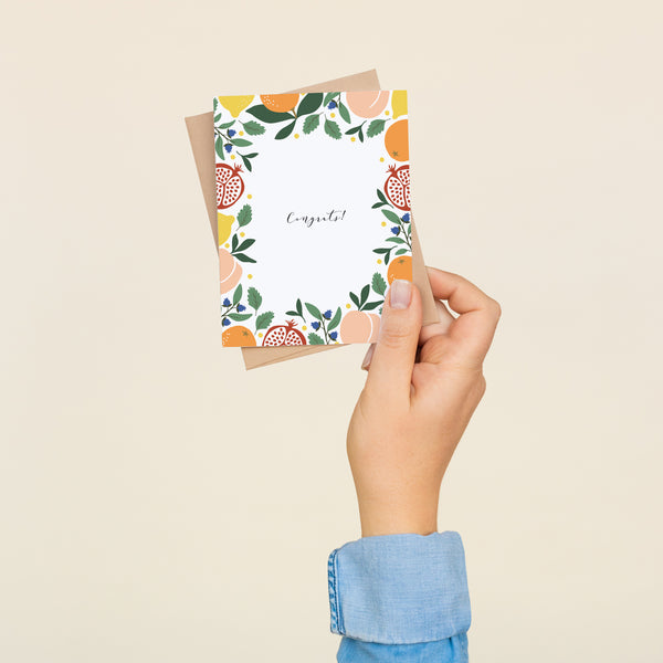 Single folded A2 greeting card with an envelope with an illustration of peaches, blueberries, lemons, pomegranates, and oranges bordering the edge of the card and the center stating "Congrats!".